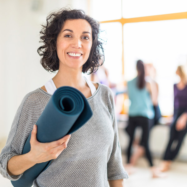 Happy mature woman holding a yoga mat in health club