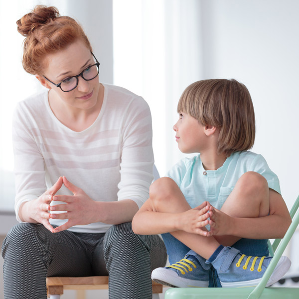 Young female school psychologist having serious conversation with smart little boy at office